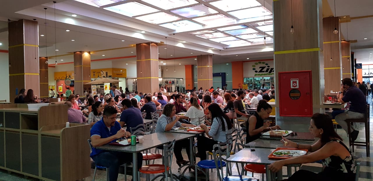 Praça de alimentação do mall do SIA Centro Empresarial com mesas ocupadas no horário de almoço