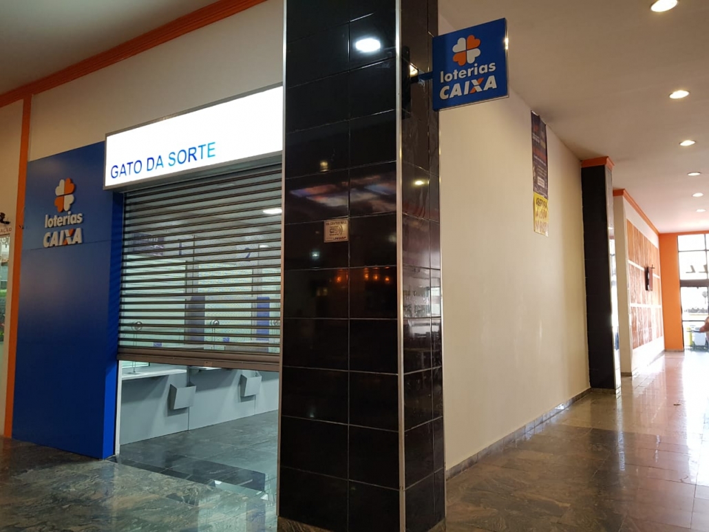 Corredor do mall com unidade de casa lotérica e sinalização de lojas de serviços